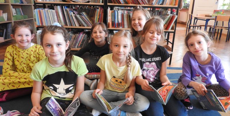 Grupa dzieci na tle regałów bibliotecznych z książkami w dłoniach