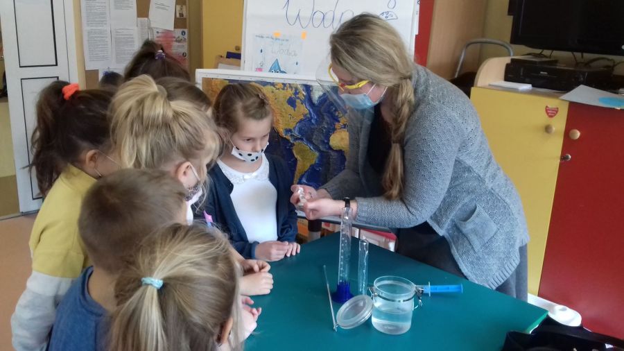 Żywioł woda-nauczyciel przedstawia dzieciom eksperyment z wodą w strzykawce