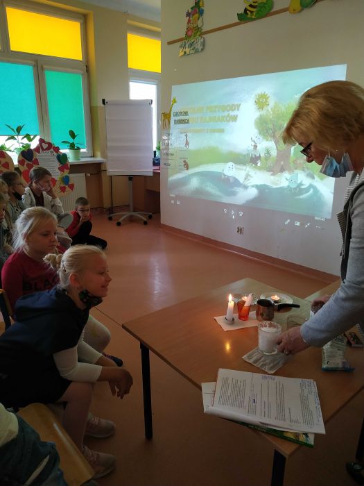 Nauczyciel przedstawia dzieciom eksperyment z Żywiołu Ogień- spalanie, w tle prezentacja multimedialna o Fajniakach.
